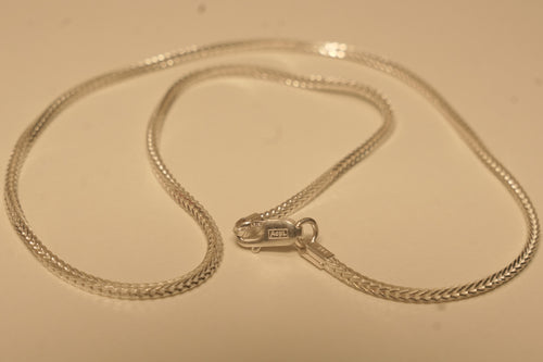 The slim silver foxtail chain coiled with the lobster clasp lying open in the middle.