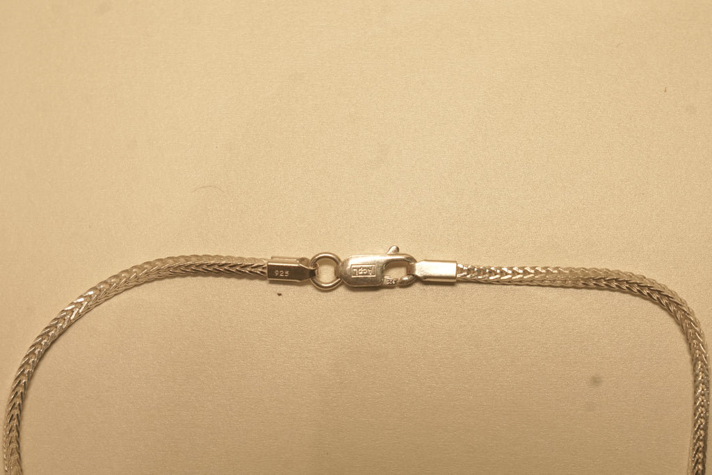 Close view of the lobster clasp on the slim silver foxtail chain, with the silver mark beside it.