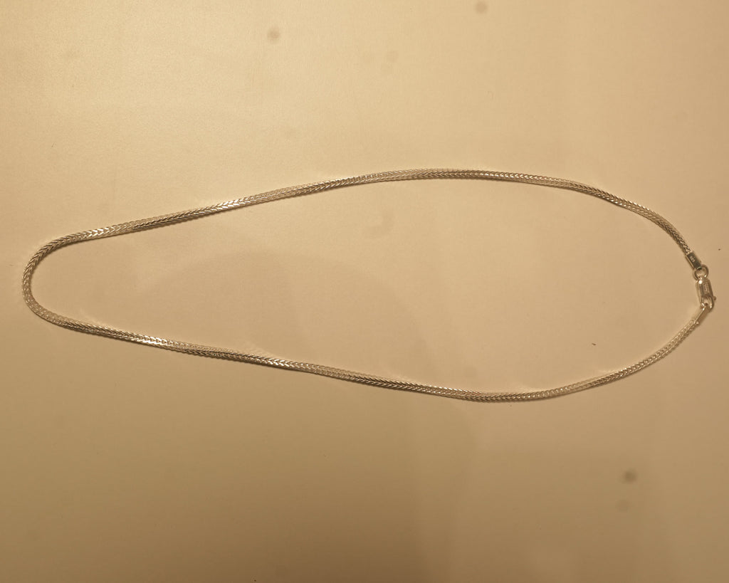 The slim silver foxtail chain laid out in a long oval to show how it falls.