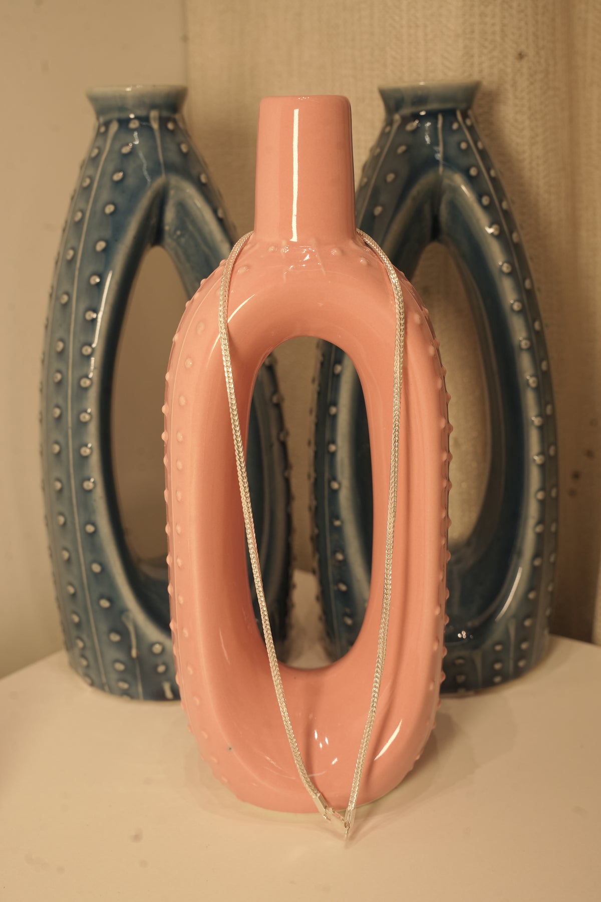The slim silver foxtail chain draped over a pink and blue ceramic vase.