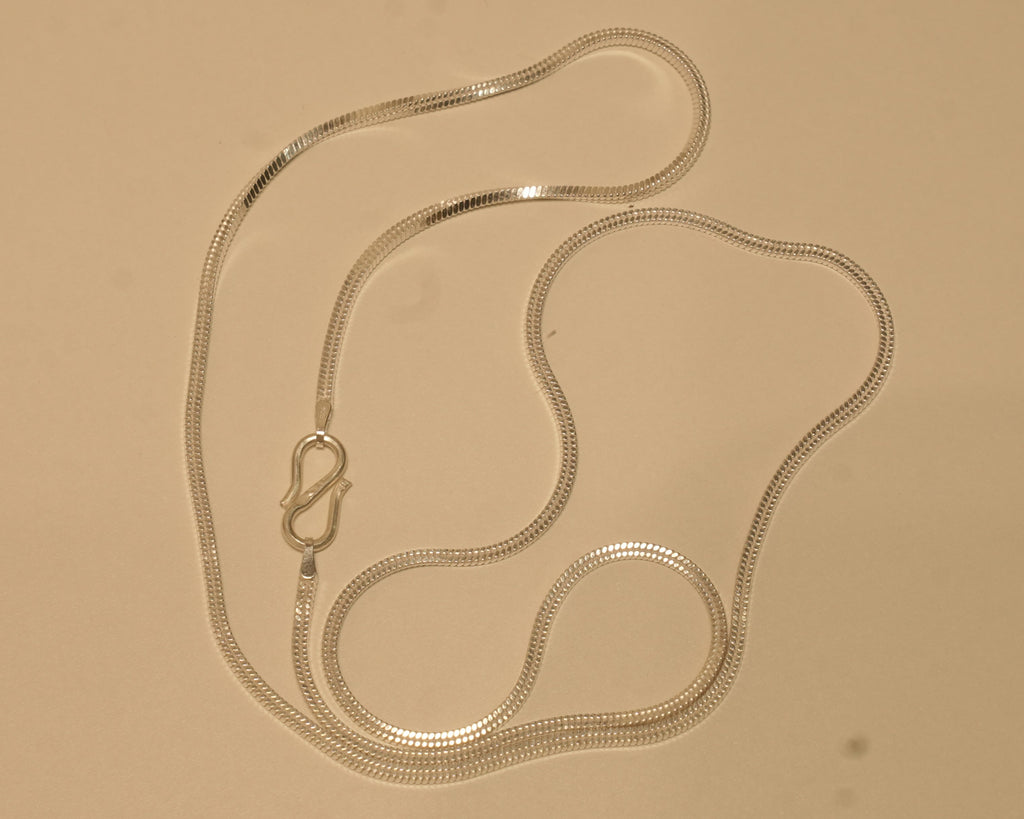 Sterling silver flat snake chain coiled on a pale surface with the S hook to one side.