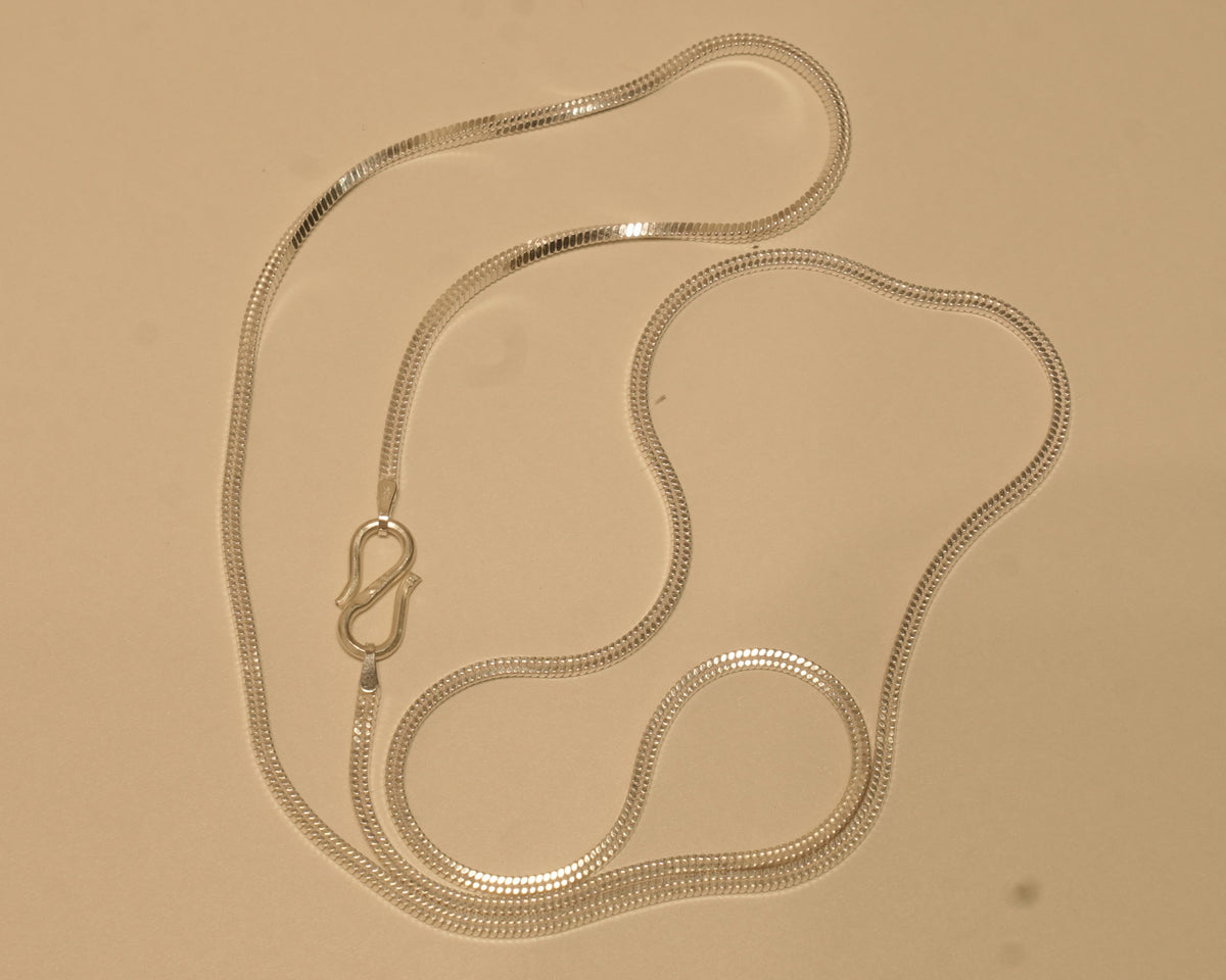 Sterling silver flat snake chain coiled on a pale surface with the S hook to one side.