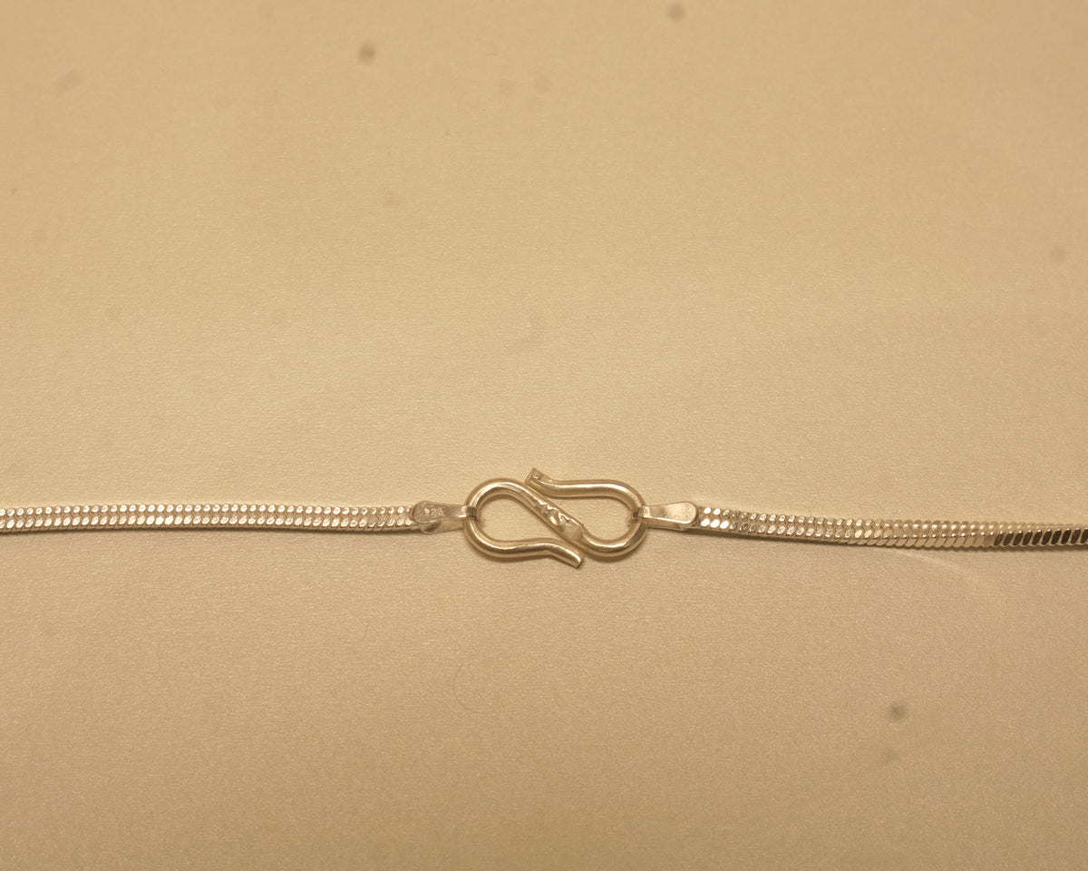 Close view of the S hook clasp joining the two ends of the silver flat snake chain.