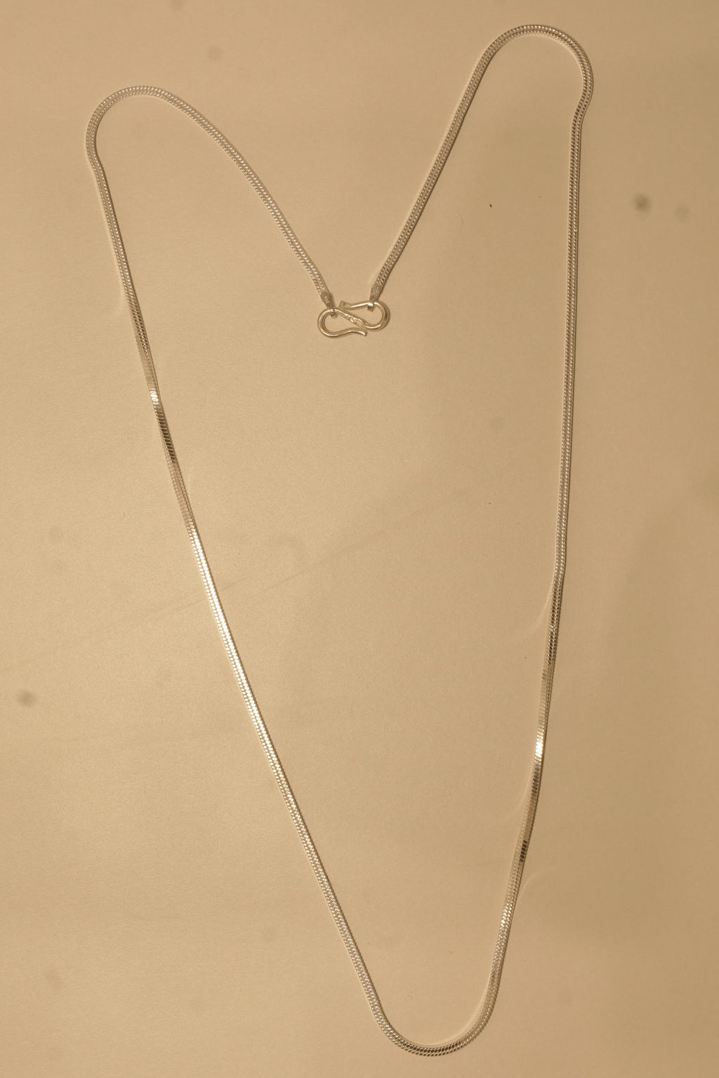 The silver flat snake chain laid out in a long V to show how it falls.