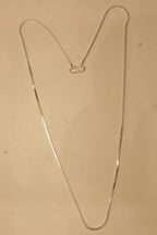 The silver flat snake chain laid out in a long V to show how it falls.
