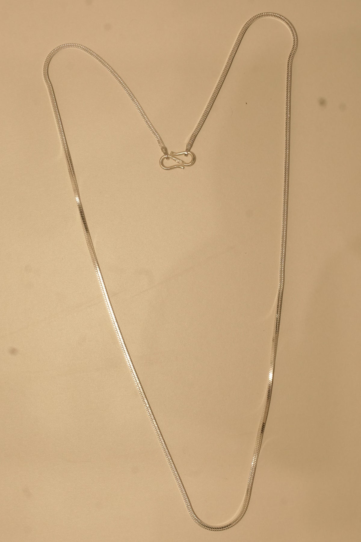 The silver flat snake chain laid out in a long V to show how it falls.