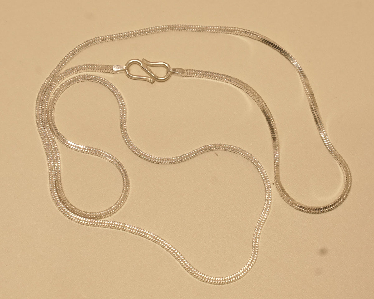 The silver flat snake chain coiled loosely with the S hook near the top.