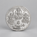 10 gram fine silver coin with Lakshmi on a lotus between Ganesh and Saraswati, on a grey surface.