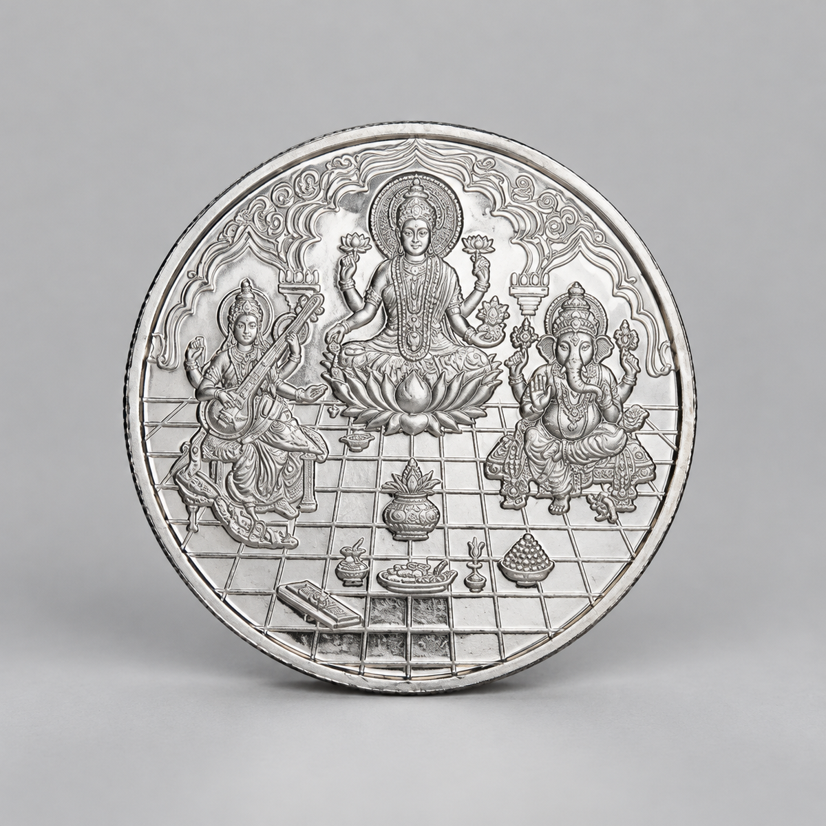 10 gram fine silver coin with Lakshmi on a lotus between Ganesh and Saraswati, on a grey surface.