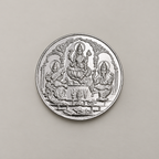 20 gram fine silver coin with Lakshmi, Ganesh and Saraswati under temple arches, on a beige surface.