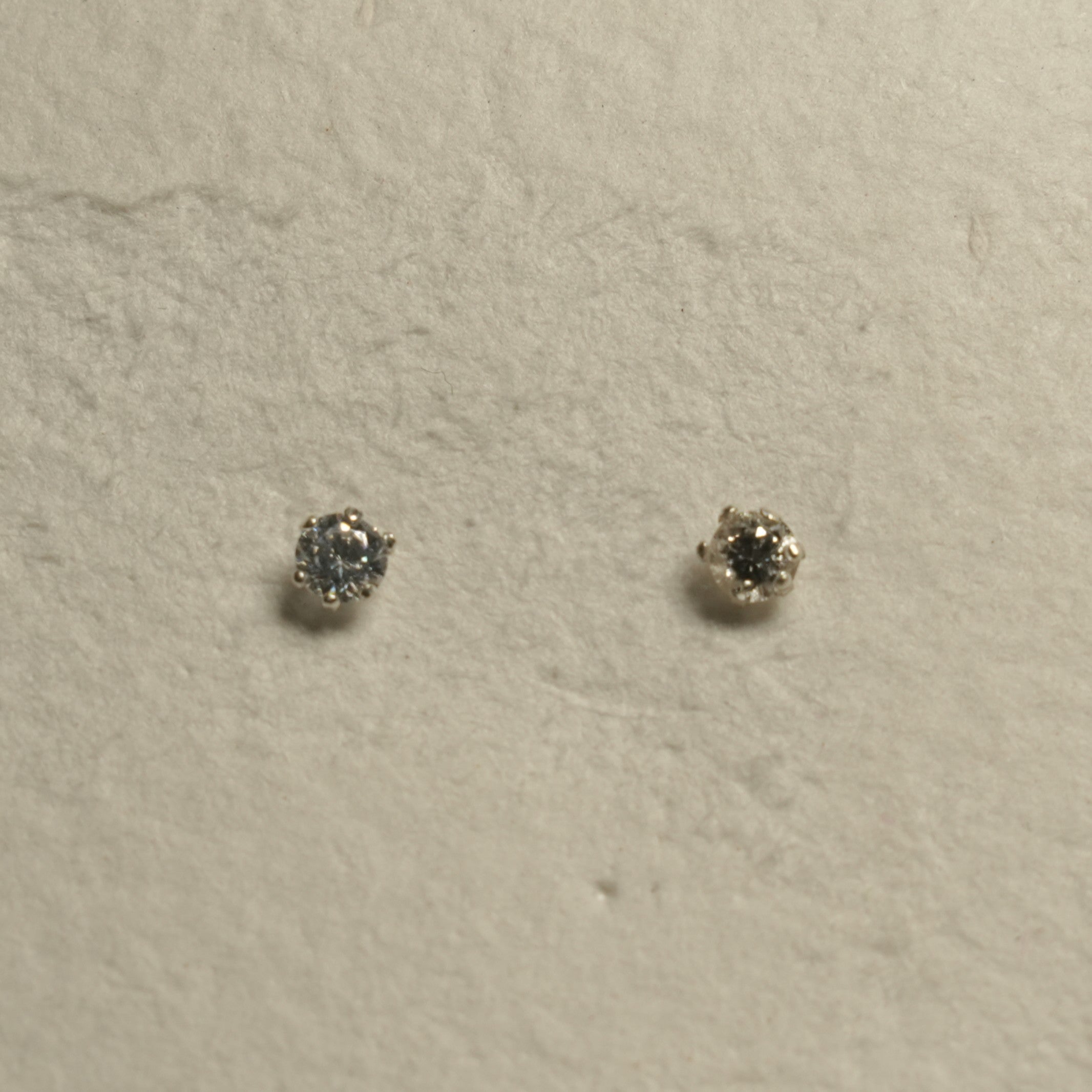 Pair of small round cubic zirconia solitaire stud earrings in prong-set sterling silver on handmade paper.