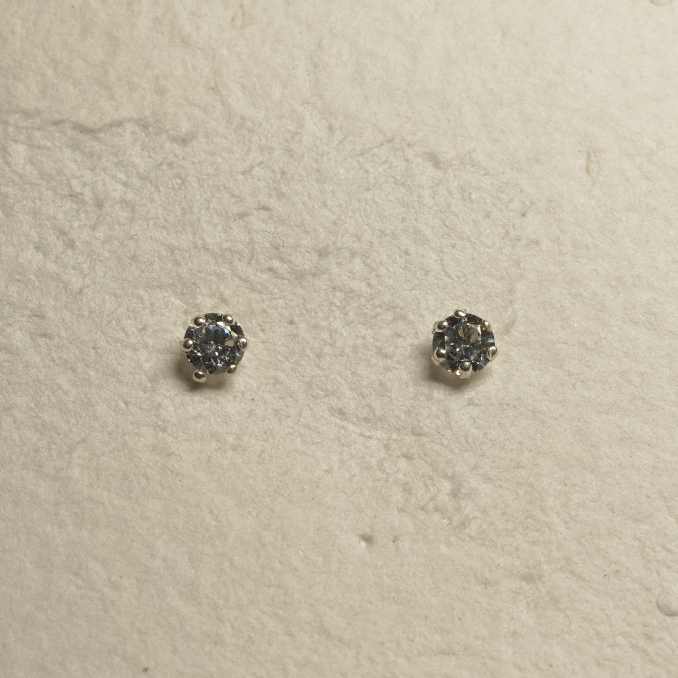 Two prong-set cubic zirconia stud earrings in sterling silver photographed side by side on textured paper.