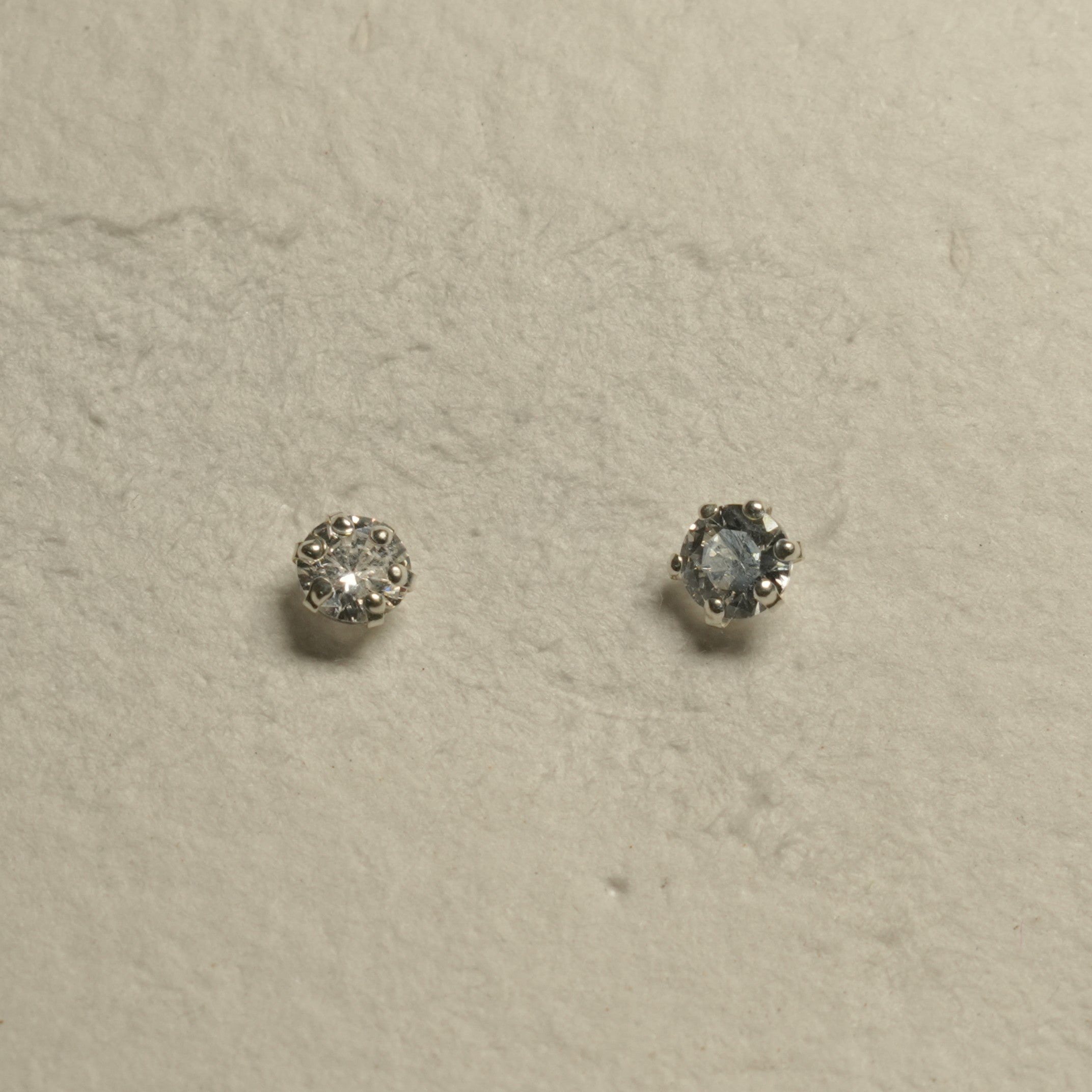 Pair of round cubic zirconia solitaire studs in sterling silver prong settings, one showing the side of its setting.