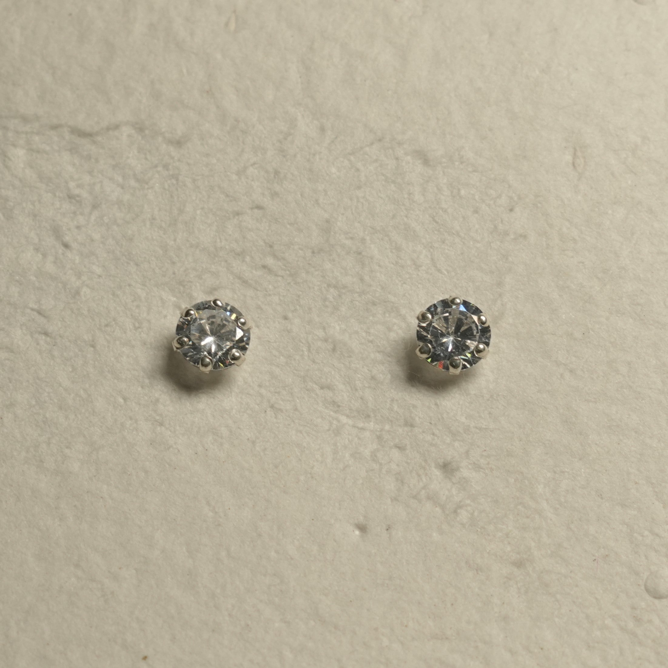 Round brilliant-cut cubic zirconia stud earrings in prong-set sterling silver arranged on handmade paper.