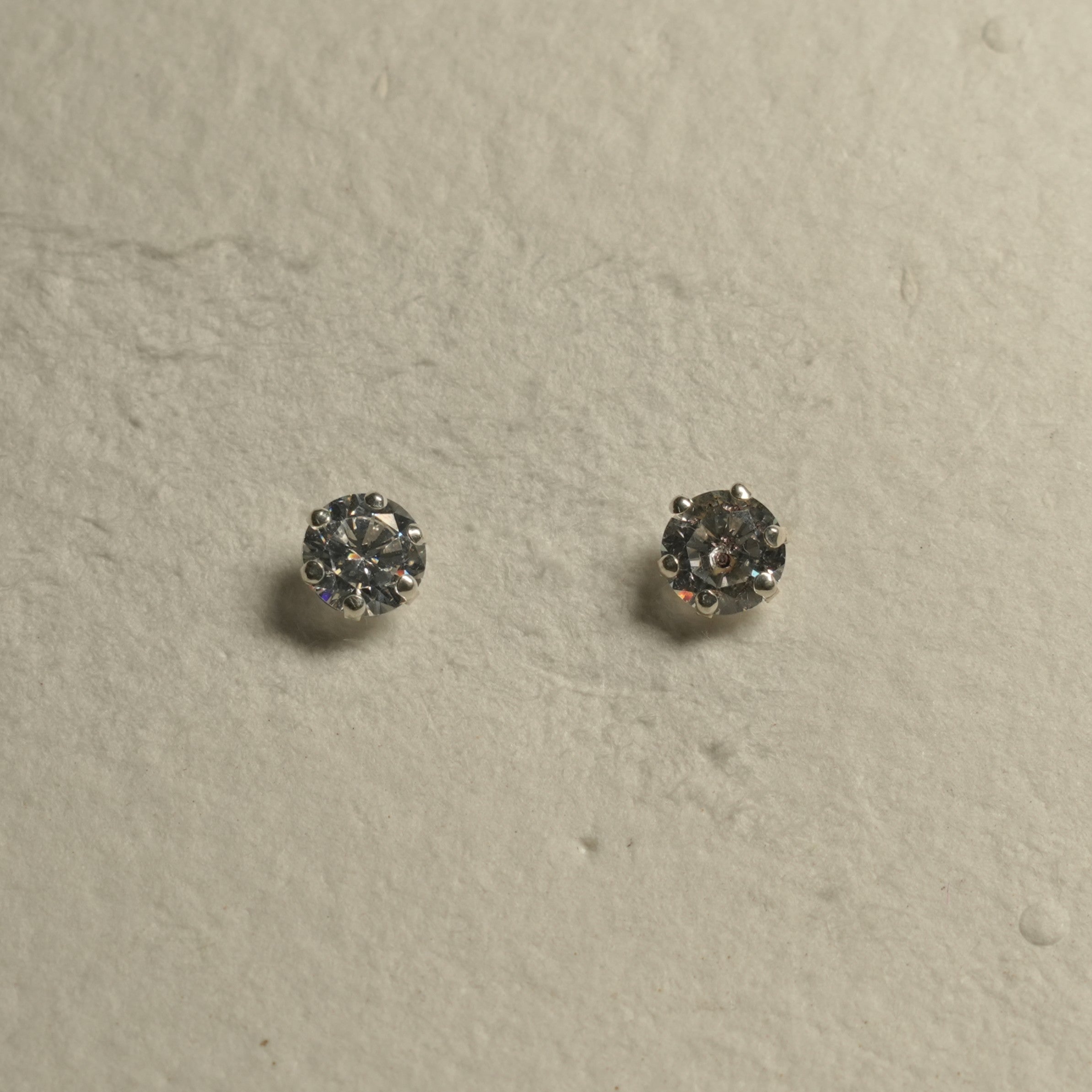 Pair of large round cubic zirconia solitaire studs in sterling silver prong settings on pale textured paper.