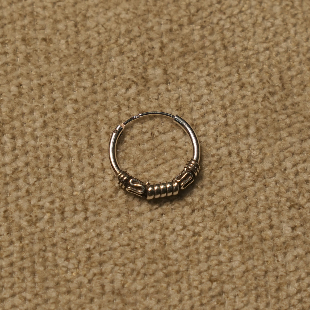 Single sterling silver Bali hoop resting on beige fabric, showing the coil and scroll handwork.