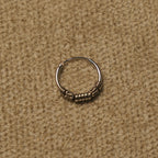 Single sterling silver Bali hoop resting on beige fabric, showing the coil and scroll handwork.
