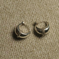 Pair of polished sterling silver dome hoop earrings with a rope-textured band across the front, resting on beige woven fabric.