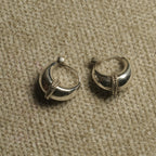 Pair of polished sterling silver dome hoop earrings with a rope-textured band across the front, resting on beige woven fabric.