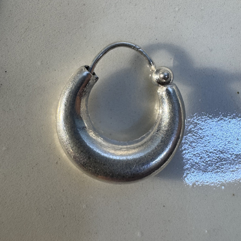 The large plain silver kundal hoop earring on a pale surface.