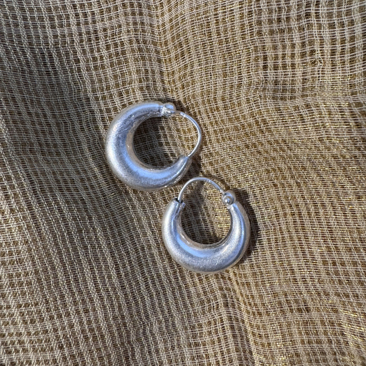 Pair of small plain sterling silver kundal hoop earrings, on cream fabric.