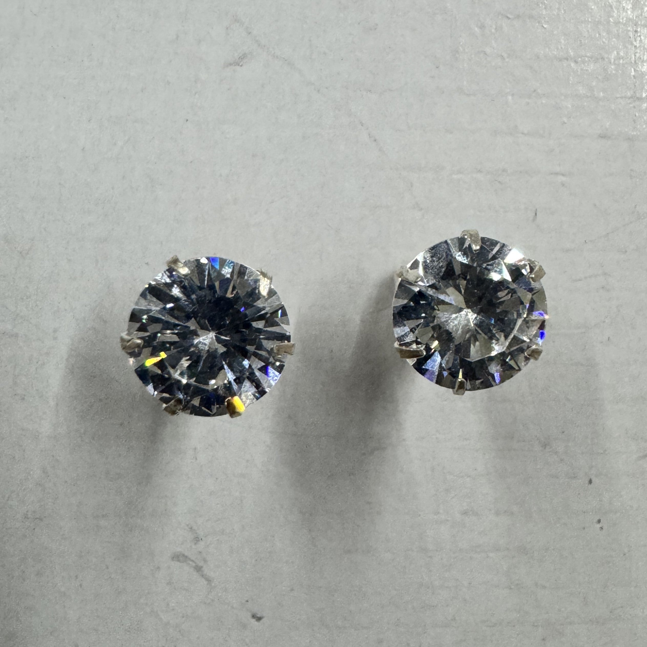 Pair of sterling silver stud earrings, each holding a round brilliant-cut cubic zirconia in a claw setting, on a pale grey surface.