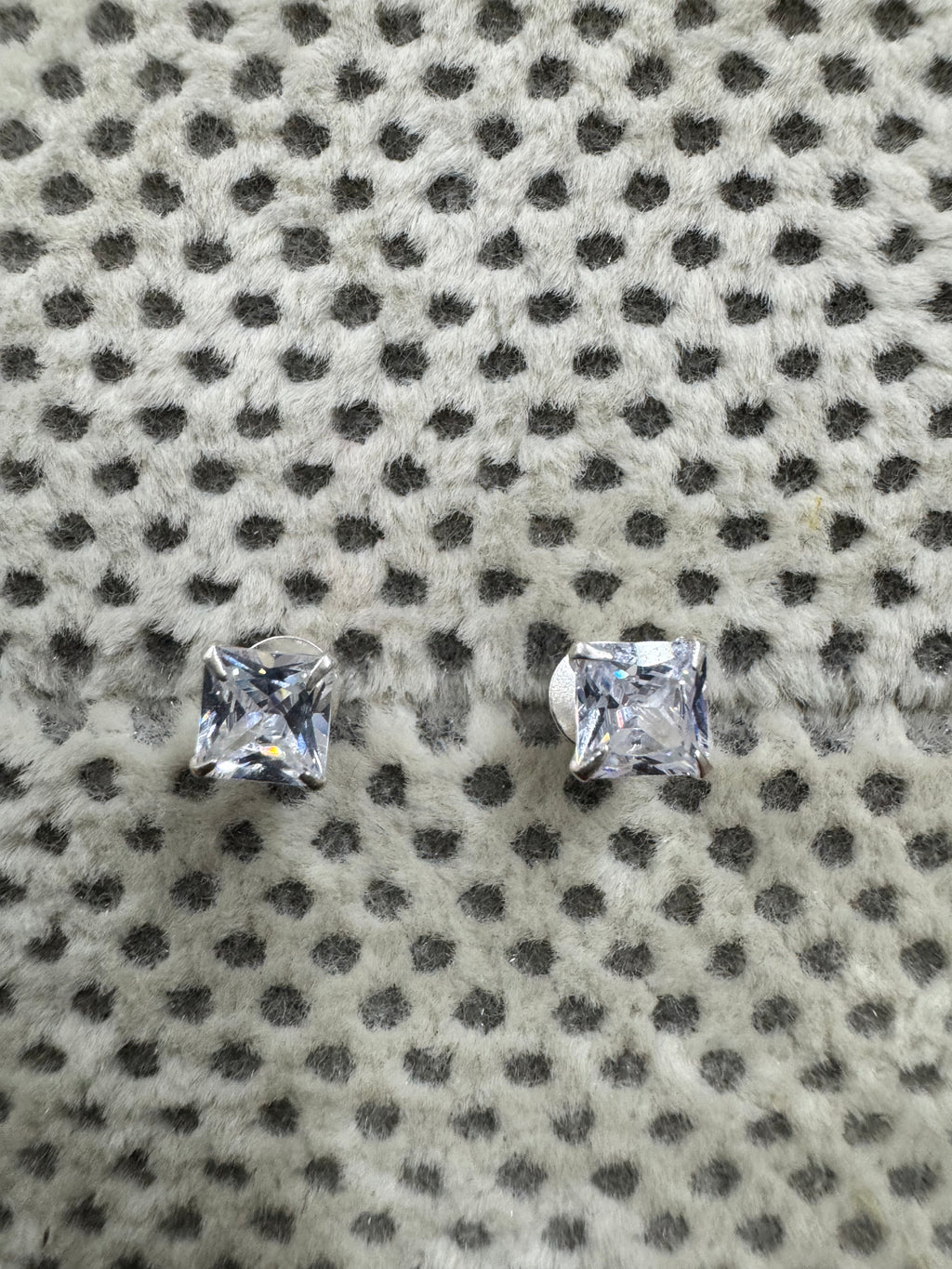 Pair of sterling silver stud earrings, each set with a square cubic zirconia, resting on spotted grey fabric.