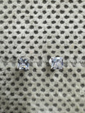 Pair of sterling silver stud earrings, each set with a square cubic zirconia, resting on spotted grey fabric.