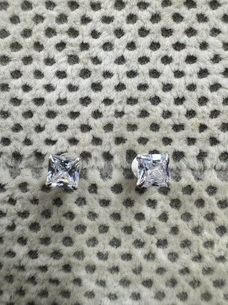 Pair of sterling silver stud earrings, each set with a square cubic zirconia, resting on spotted grey fabric.