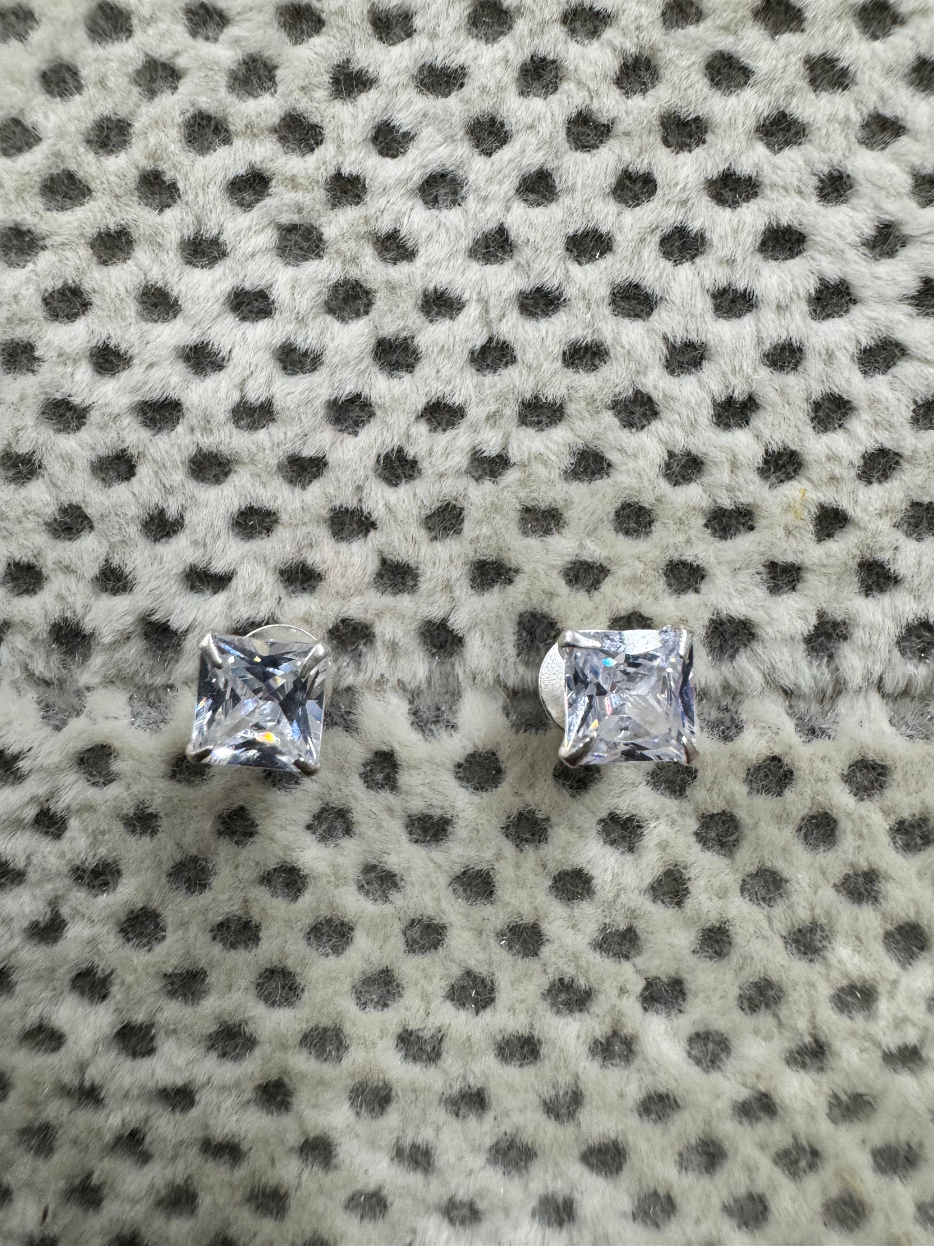 Pair of sterling silver stud earrings, each set with a square cubic zirconia, resting on spotted grey fabric.