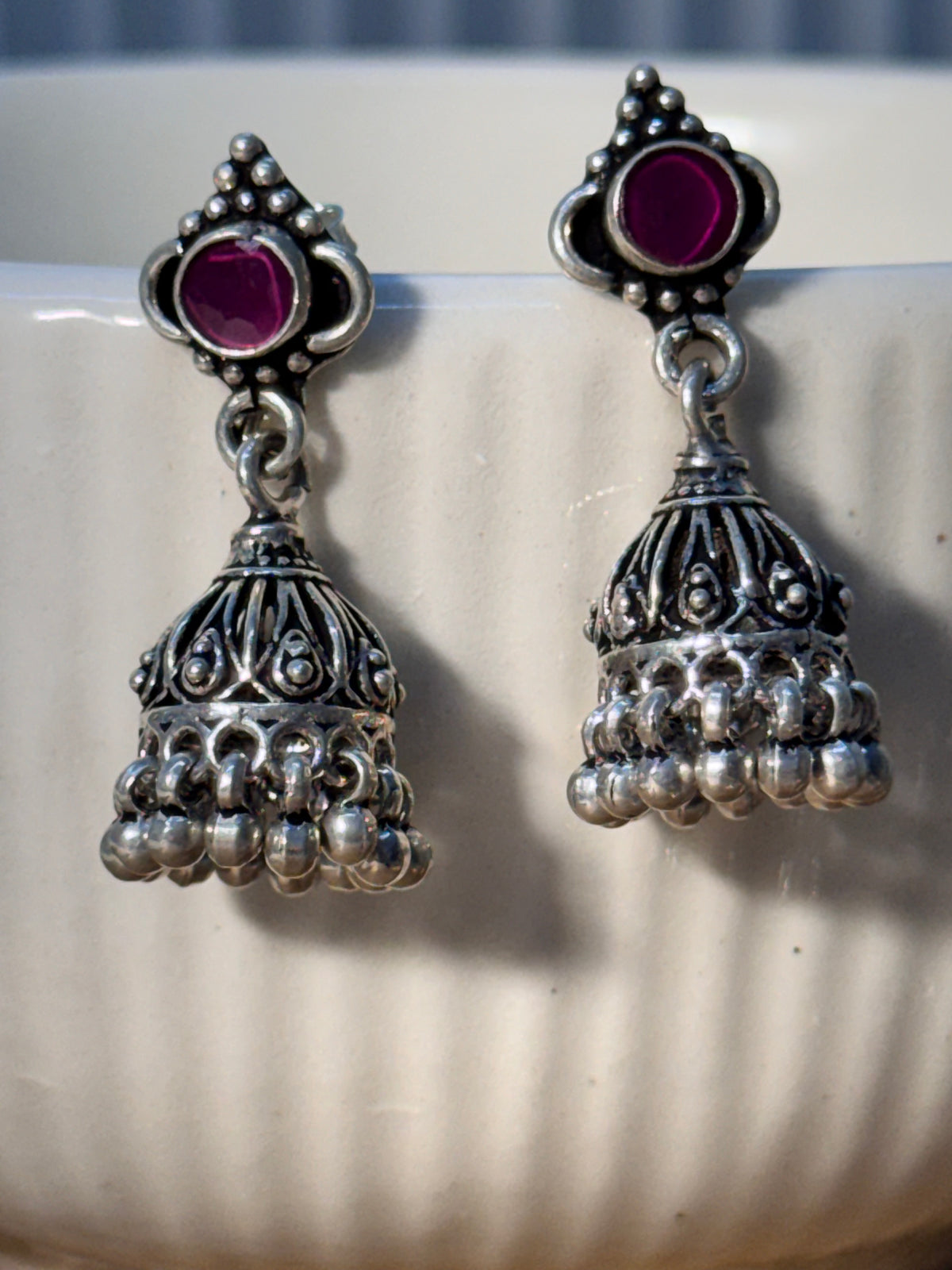 Two oxidised silver jhumka styles with pink glass stone tops shown together, the floral bead dome in front.