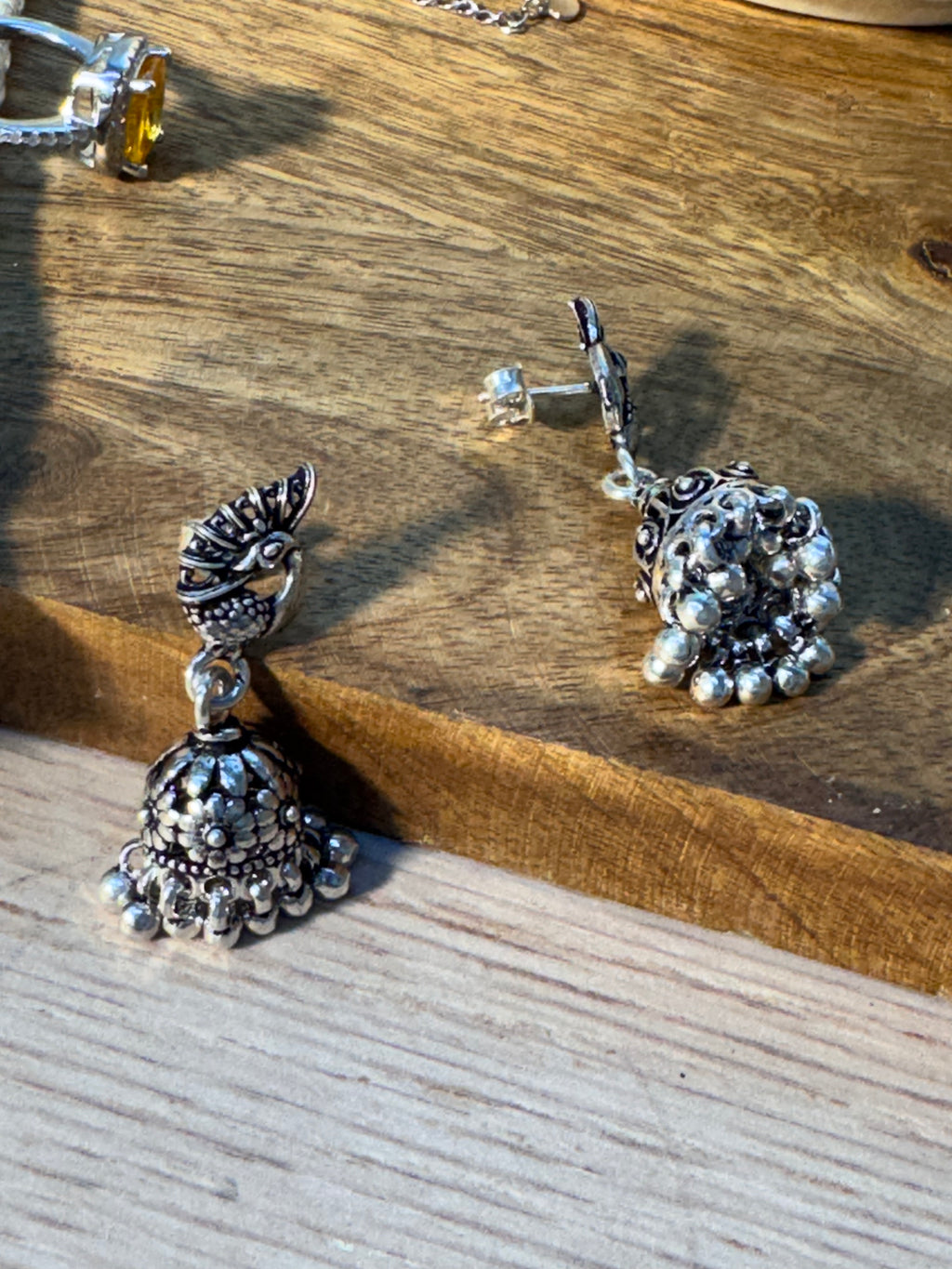 Close view of the peacock stud above the oxidised jhumka dome, showing the crest and tail detail.