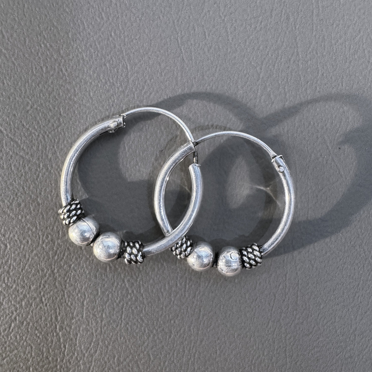 The pair of silver Bali hoops lying one over the other on a grey surface.