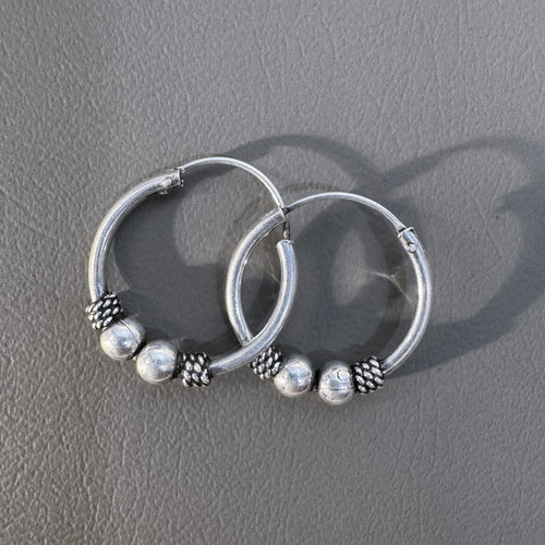 The pair of silver Bali hoops lying one over the other on a grey surface.