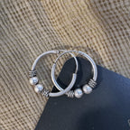 The Bali hoop earrings on cream fabric with the Javeri House card behind.