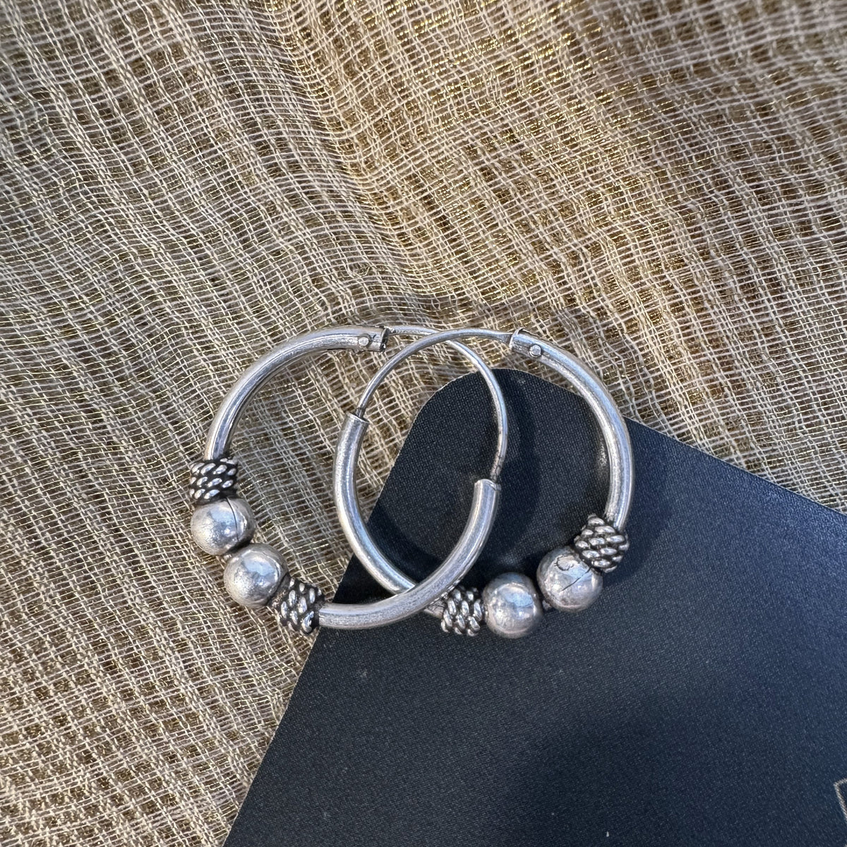 The Bali hoop earrings on cream fabric with the Javeri House card behind.