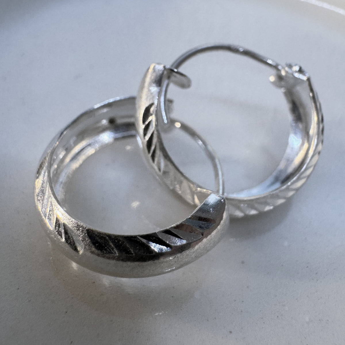 Pair of sterling silver diamond-cut hoop earrings resting on a white dish.