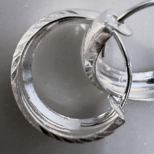 Close view of the faceted edges and the hinged closure of the silver hoops.