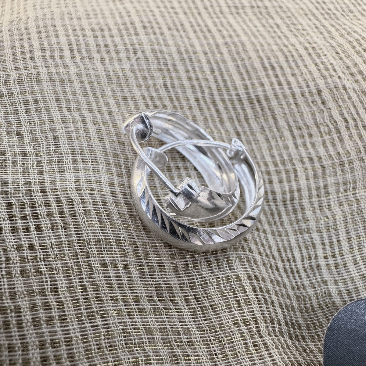The pair of diamond-cut silver hoops on cream fabric.