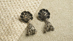 Pair of oxidised sterling silver peacock jhumka earrings with teardrop cutwork tops and beaded bell drops, on ivory woven fabric.