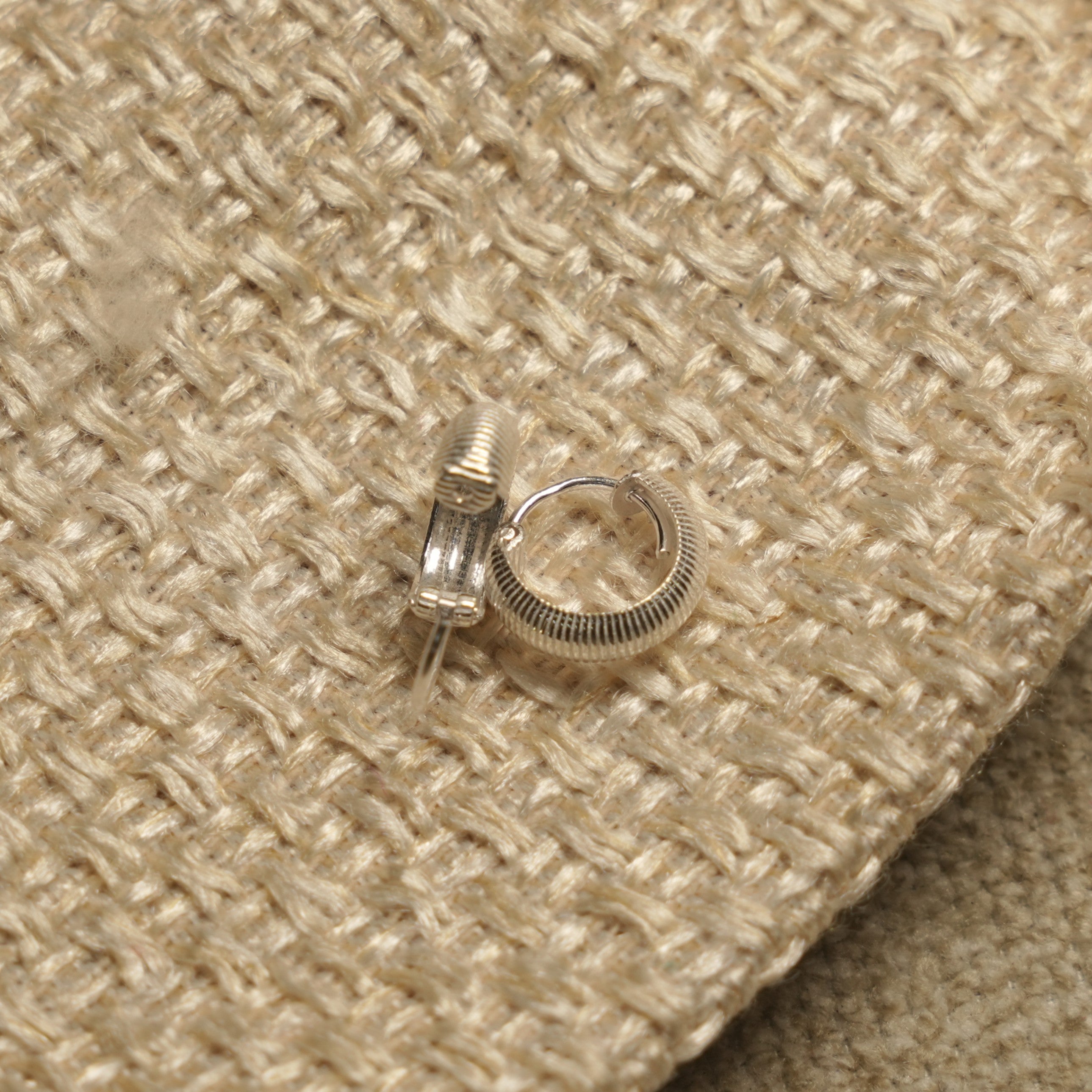 Close view of the ribbed sterling silver huggie hoops, one open to show the hinged closure.