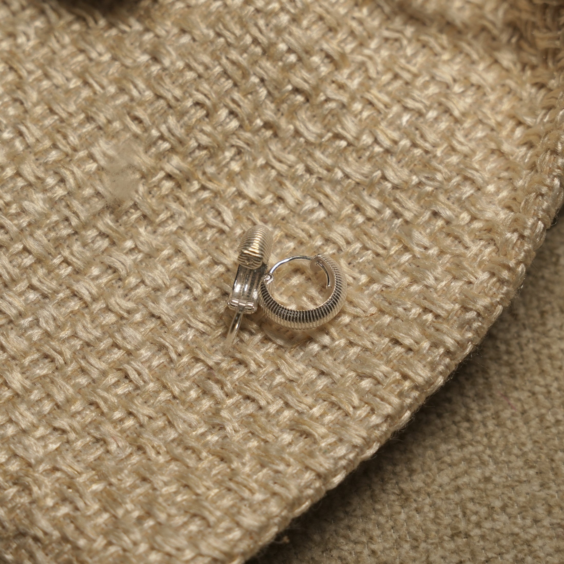 Ribbed sterling silver huggie hoop earrings shown against a natural woven jewellery pouch.