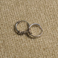 Pair of sterling silver Bali-style hoop earrings with coiled wire and scroll detailing, resting on beige fabric.