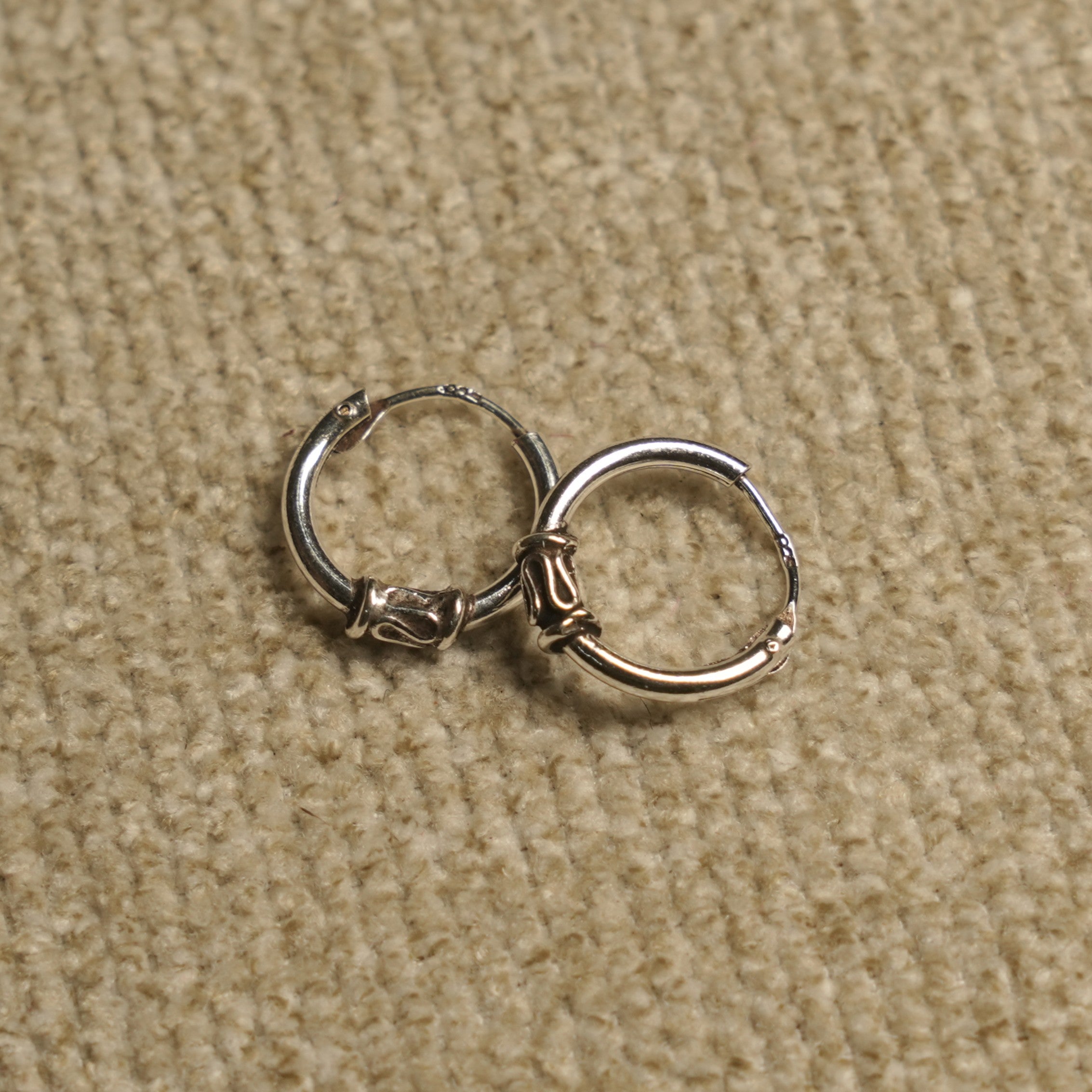 Pair of sterling silver Bali-style hoop earrings with coiled wire and scroll detailing, resting on beige fabric.