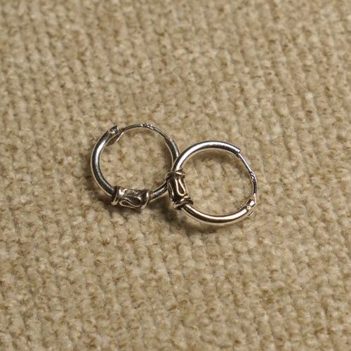 Pair of sterling silver Bali-style hoop earrings with coiled wire and scroll detailing, resting on beige fabric.