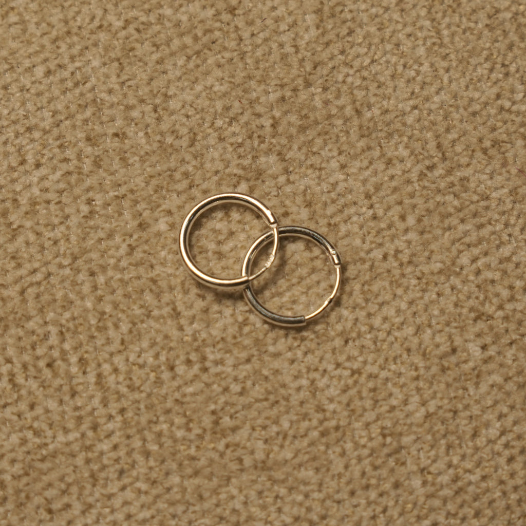 Pair of slim polished sterling silver hoop earrings overlapping on beige fabric.