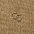 Pair of slim polished sterling silver hoop earrings overlapping on beige fabric.