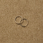 Pair of slim polished sterling silver hoop earrings overlapping on beige fabric.