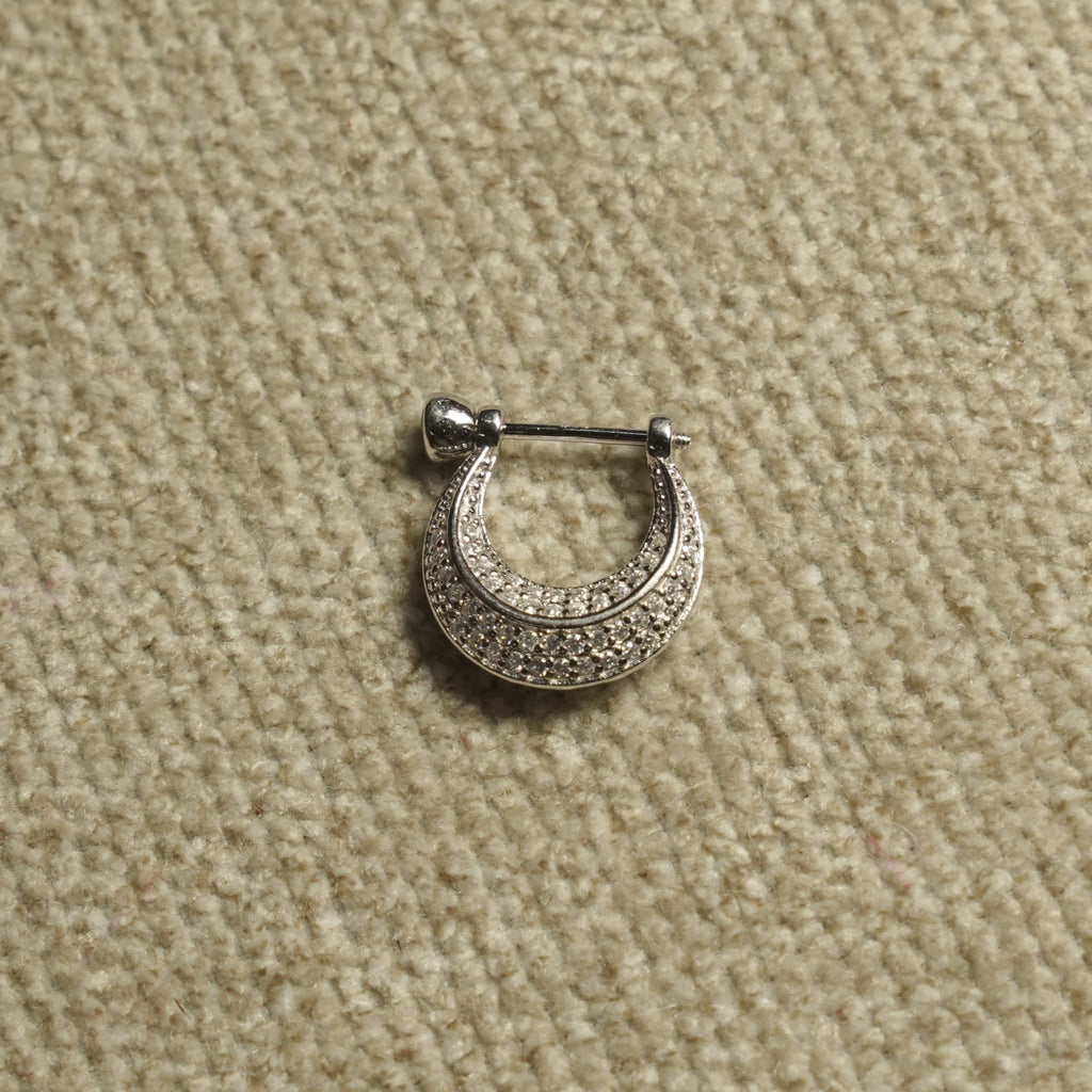Single sterling silver Bejewelled crescent hoop earring shown up close, its rows of cubic zirconia following the curve, on beige woven fabric.