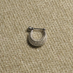 Single sterling silver Bejewelled crescent hoop earring shown up close, its rows of cubic zirconia following the curve, on beige woven fabric.